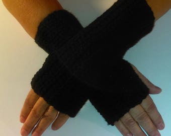 May include: A pair of black fingerless gloves, hand-knitted with a textured stitch. The gloves cover the wrists and extend partially up the forearms. The dark colour and simple design suggest a versatile accessory for cooler weather.