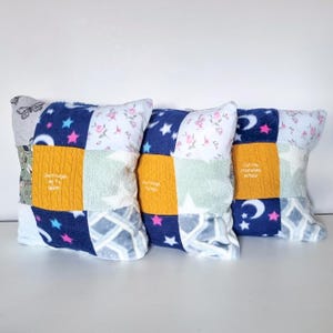 May include: Three patchwork pillows with a blue, white, and yellow color scheme. The pillows are made from different fabrics, including fleece, cotton, and knit. The pillows have embroidered text that says "Don't forget me" and "Catch me snuggles in your arms".