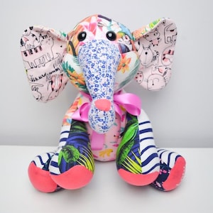 May include: A vibrant patchwork elephant soft toy. The elephant has a blue floral trunk, pink ears with animal drawings, and a pink ribbon. The feet display a mix of patterns, including stripes and tropical leaves.