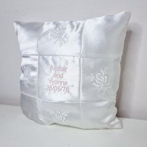 May include: White satin pillow with embroidered roses and the text "Alistair and Yvonne 28/05/76" in pink thread.