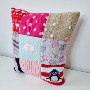 May include: A patchwork pillow with a variety of colors and textures, including pink, red, blue, and brown. The pillow has a penguin applique on one side and the name "Lexie Lou" embroidered on the other side.
