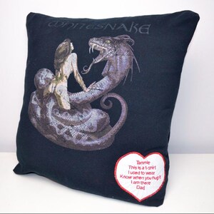 May include: Black cushion with a graphic of a woman and a snake, and the band name "Whitesnake" above. A heart-shaped patch with text is sewn on the bottom right. A unique home decor item.