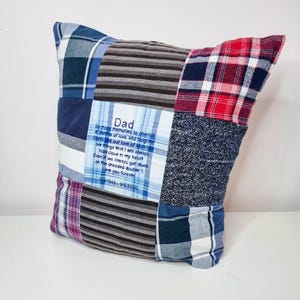 May include: A patchwork pillow with a blue and white plaid fabric, a red and white plaid fabric, a gray and white striped fabric, and a blue and gray fabric. The pillow has a blue square in the center with the text "Dad" and a poem about memories and love.