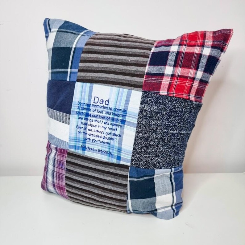 May include: A patchwork pillow with a blue and white plaid fabric, a red and white plaid fabric, a gray and white striped fabric, and a blue and gray fabric. The pillow has a blue square in the center with the text "Dad" and a poem about memories and love.