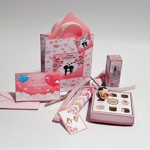 May include: A miniature Valentine's Day gift set featuring a pink gift bag with heart patterns, a card with a heart balloon, a box of chocolates, a perfume bottle, and a small envelope. The set includes a ribbon and a small rose.