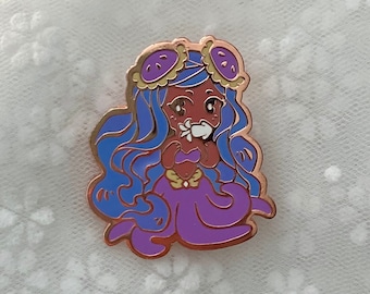 May include: A purple and blue enamel pin of a cartoon mermaid with a flower in her hand. She has brown skin, blue hair, and wears a gold crown and a purple seashell top.