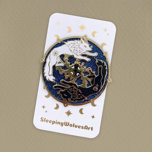 May include: Gold enamel pin featuring a white wolf and a black wolf facing each other in a circle. The wolves are surrounded by a blue glitter background with stars and moons. The pin says "SleepingWolvesArt" at the bottom.