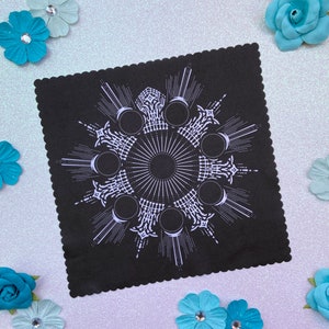 Könnte beinhalten: Schwarzes Stoffquadrat mit einem weißen Mondphasen-Mandala-Design. Das Design zeigt einen Kreis mit acht Mondphasen und einen nach außen strahlenden Sonnenstrahl.