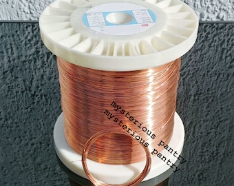 May include: A spool of copper wire, wound tightly on a white plastic spool. The wire is shiny and has a reddish-brown color. A small loop of the wire is shown in the foreground.