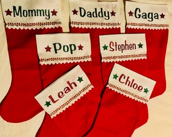 May include: Six red Christmas stockings with white cuffs and colorful trim. The stockings are personalized with names including "Mommy", "Daddy", "Gaga", "Pop", "Stephen", and "Chloe".
