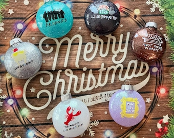 May include: Six glittery Christmas baubles with a Friends TV show theme. The baubles are silver, blue, purple, white, and pink. The baubles have text on them, including "Friends", "Pivot, Pivot, Pivot", "You're My Lobster", "How You Doin'" and "I'll Be There For You".