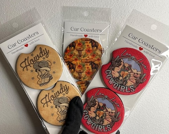 May include: Car coasters with western-themed designs. One set features the word "Howdy" with a cowboy graphic. Another set has a floral and horse pattern. The third set has "Long Live Cowgirls" with a desert scene.