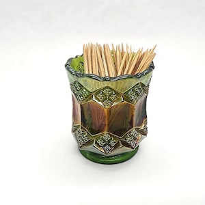 May include: A dark green iridescent glass toothpick holder with a scalloped rim and a geometric diamond pattern featuring embossed floral details. The cylindrical vessel is filled with numerous light brown wooden toothpicks.