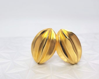 May include: A pair of gold-toned earrings with a ridged, oval shape.
