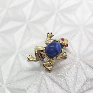 May include: A gold frog brooch with a blue swirl glass stone and red rhinestone eyes.