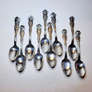 May include: A set of ten silver teaspoons with ornate handles. Each spoon has a different design featuring a crown and other decorative elements.