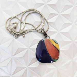 May include: A silver chain necklace with a pendant featuring a colorful abstract design. The pendant is oval-shaped and has a dark blue background with orange, yellow, and green accents.