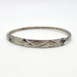 May include: A silver bangle bracelet with a diamond pattern on the front. The bracelet has a hinged clasp.