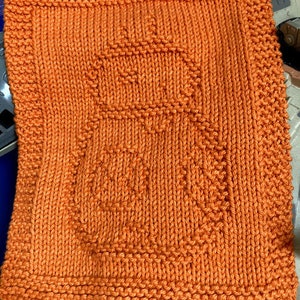 May include: A bright orange knitted dishcloth with a geometric pattern. The dishcloth is made of cotton yarn and is ideal for washing dishes or drying hands.