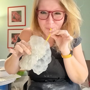 Peut inclure: Un moule en silicone translucide &agrave; la texture alv&eacute;ol&eacute;e en forme de grappe de raisin, tenu en main tandis qu'une paille jaune est utilis&eacute;e pour souffler de l'air &agrave; la surface afin de cr&eacute;er de la mousse. Le moule est souple et transparent.