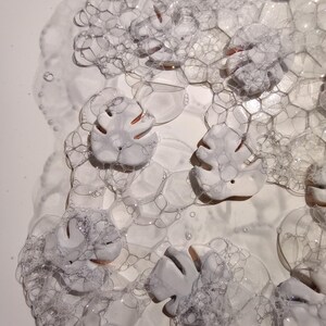 Peut inclure: Une collection de pi&egrave;ces en c&eacute;ramique blanche en forme de feuilles avec des d&eacute;tails d&eacute;coup&eacute;s, partiellement immerg&eacute;es sous une &eacute;paisse couche de bulles de savon translucides. Les feuilles ont une finition mate et lisse.