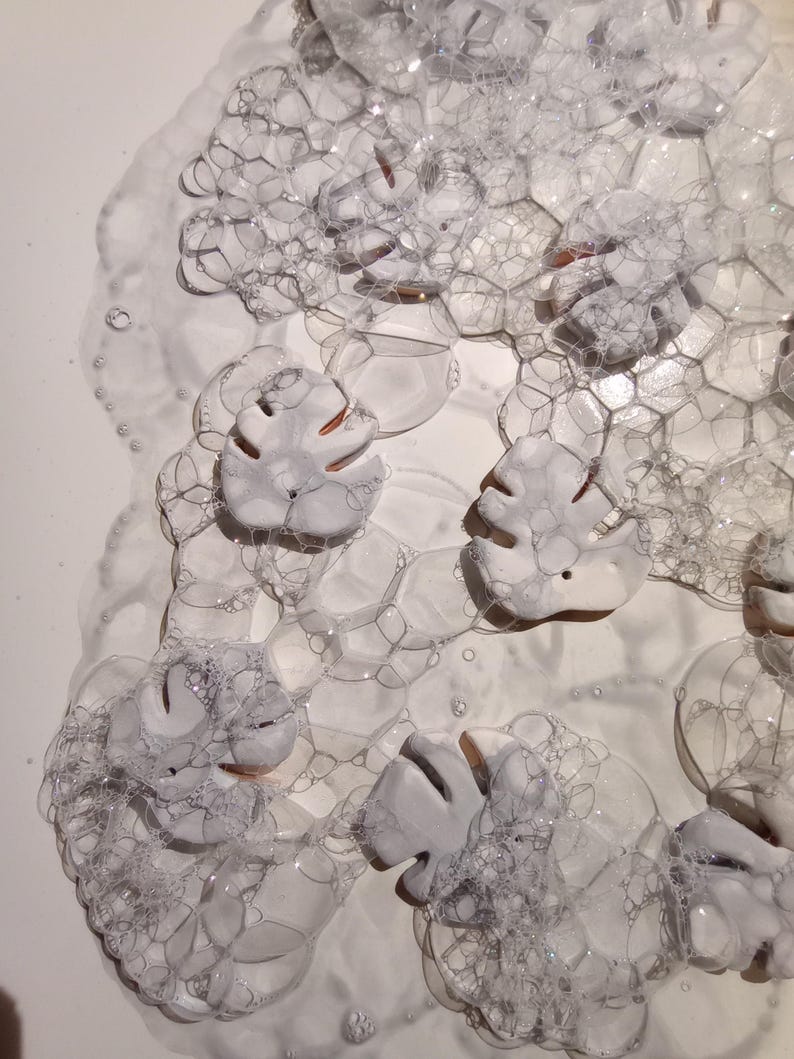 Peut inclure: Une collection de pi&egrave;ces en c&eacute;ramique blanche en forme de feuilles avec des d&eacute;tails d&eacute;coup&eacute;s, partiellement immerg&eacute;es sous une &eacute;paisse couche de bulles de savon translucides. Les feuilles ont une finition mate et lisse.