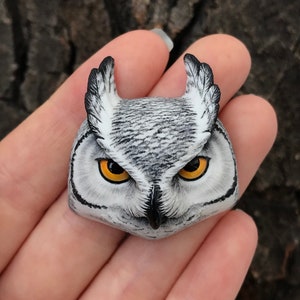 May include: A hand-painted owl figurine with realistic details, featuring a white and gray body with black markings and bright yellow eyes.