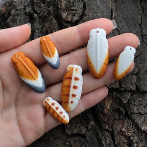 May include: Six ceramic feather charms in various colours, including white, orange, and brown. The feathers have a realistic appearance and are perfect for jewellery making or crafting.