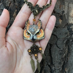 Puede incluir: Un collar de b&uacute;ho marr&oacute;n y dorado con un colgante de b&uacute;ho detallado, cuentas de color &aacute;mbar y una cadena de bronce. El b&uacute;ho tiene ojos y plumas realistas.