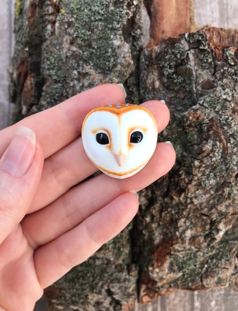 May include: A small ceramic owl figurine with brown and white markings. The owl has black eyes and a white beak.