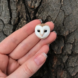 May include: A small, white and brown owl figurine with black eyes. The owl is sculpted in a realistic style and has a detailed face.