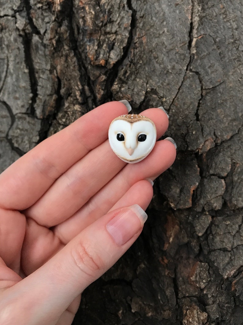May include: A small, white and brown owl figurine with black eyes. The owl is sculpted in a realistic style and has a detailed face.