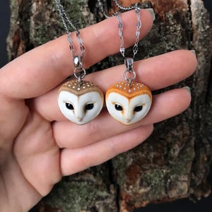 May include: Two silver chain necklaces with owl pendants. The owls are made of white and brown clay and have realistic details. One owl has orange-brown feathers and the other has white feathers.