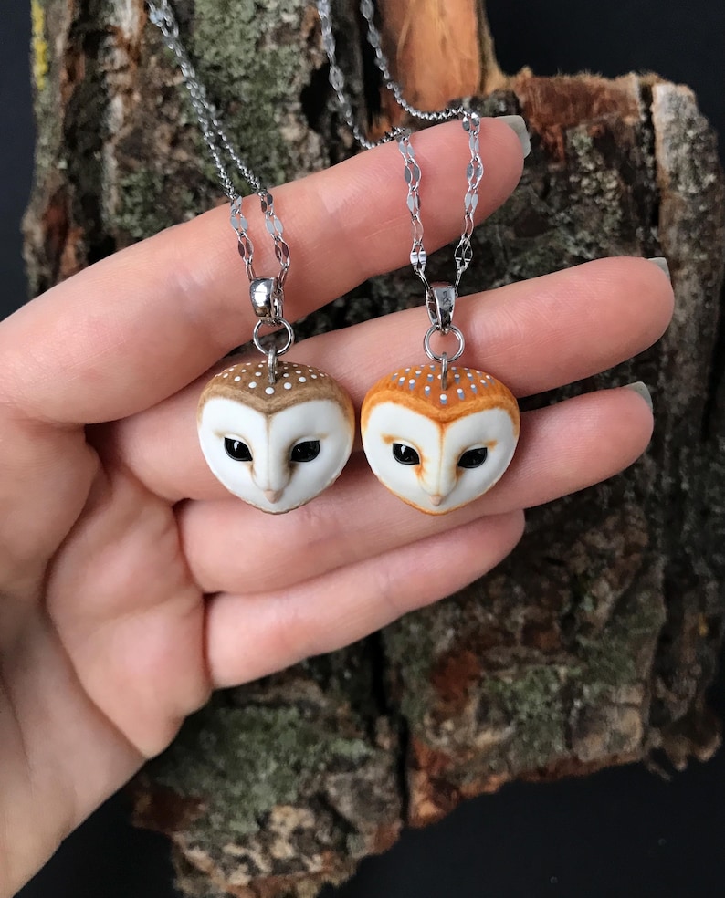 May include: Two silver chain necklaces with owl pendants. The owls are made of white and brown clay and have realistic details. One owl has orange-brown feathers and the other has white feathers.