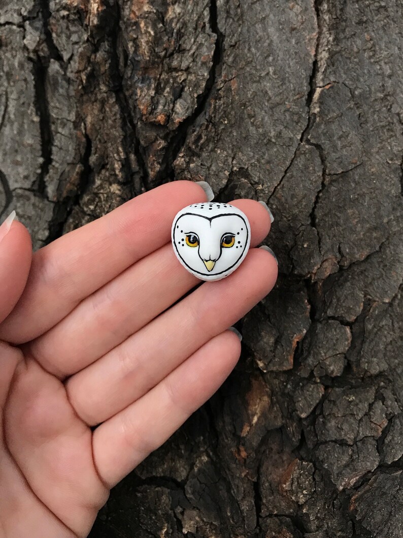 May include: A small white ceramic owl figurine with black and yellow details. The owl has black eyes and a yellow beak.