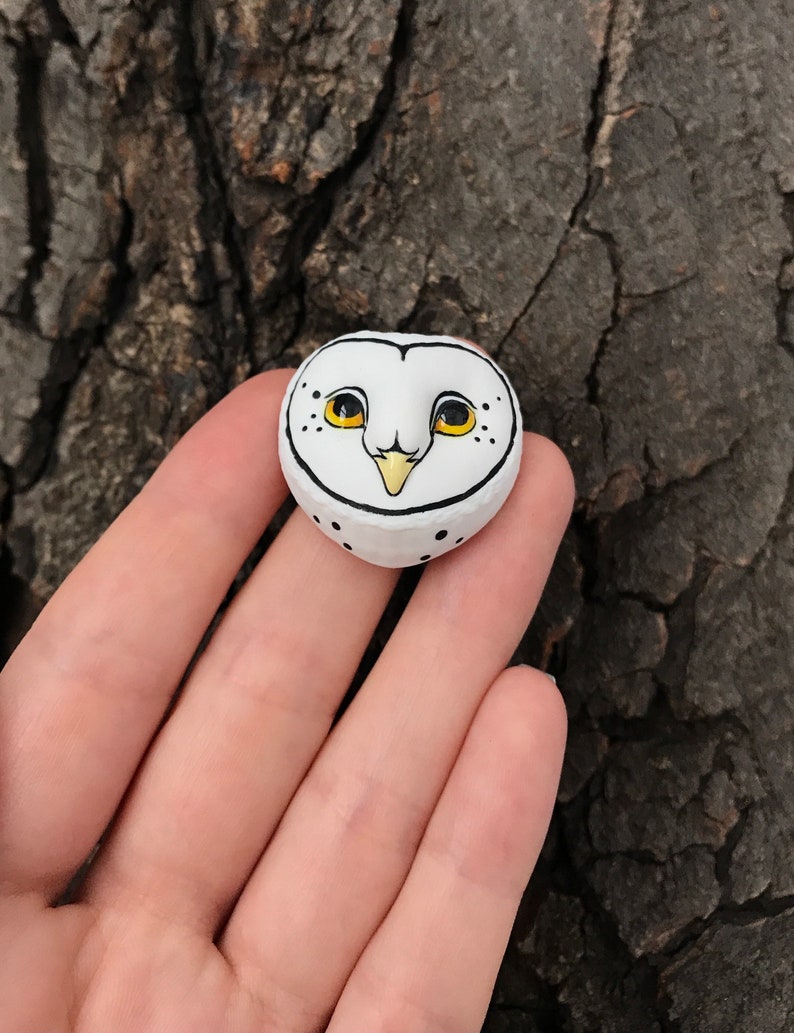 May include: A white ceramic owl figurine with black eyes and a yellow beak. The owl is painted with black dots and has a white background.