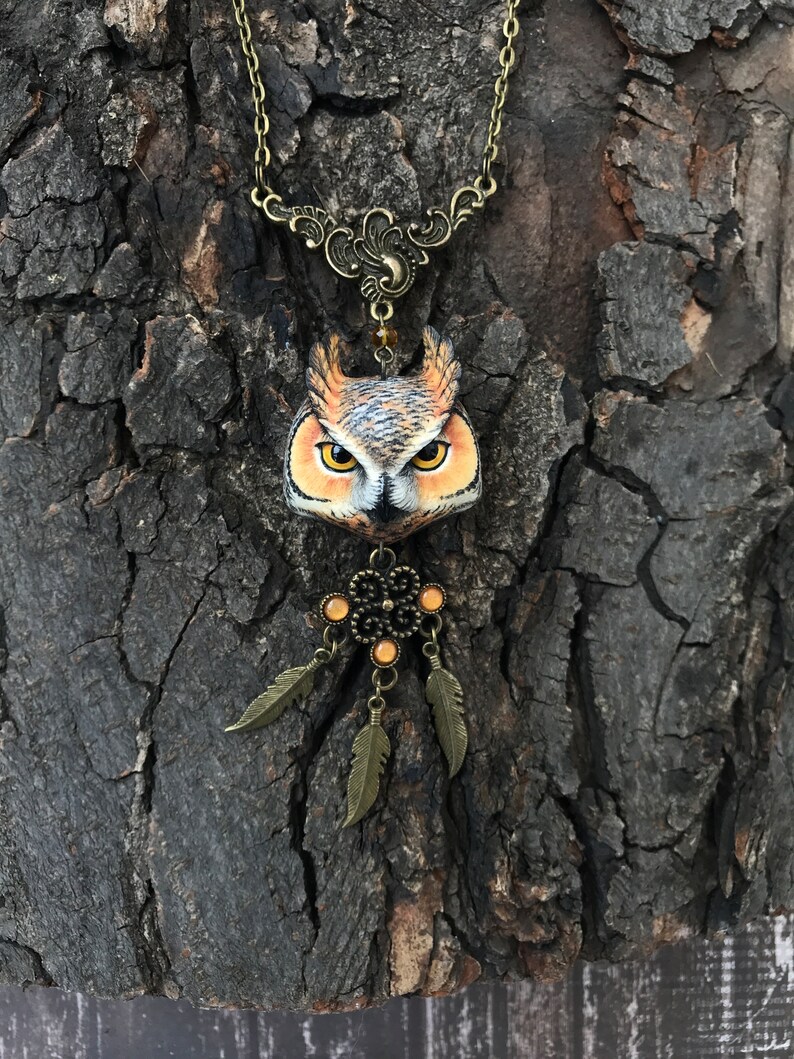 Puede incluir: Un collar con un colgante de b&uacute;ho marr&oacute;n con un dise&ntilde;o de atrapasue&ntilde;os. El b&uacute;ho tiene ojos naranjas y est&aacute; hecho de arcilla polim&eacute;rica. El collar est&aacute; hecho de cadena de bronce y tiene un amuleto de atrapasue&ntilde;os de bronce con cuentas naranjas.