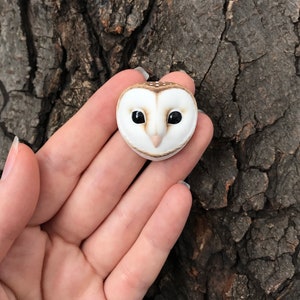 May include: A small, white and brown owl figurine with black eyes. The owl is facing forward and has a small beak.