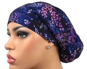 May include: A dark blue surgical scrub cap with a floral pattern in shades of purple and blue. The cap is made of soft fabric and is designed to cover the hair during medical procedures. The cap is shown on a mannequin.