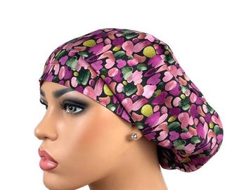 May include: A colorful scrub cap featuring a pattern of pink, purple, and green abstract shapes on a black background. The cap is designed to cover the head and hair, commonly used in medical settings.