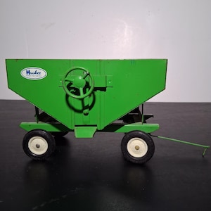 May include: Green toy wagon with a Huskee Farm Equipment logo and a black steering wheel. The wagon has two white wheels and a metal frame.