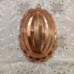 May include: A copper-colored, oval-shaped baking mold with fluted sides. The mold has a hanging loop at the top.