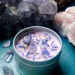 以下が含まれることがあります： 銀色の缶に入った、アメジストの結晶と乾燥ラベンダーの花が入ったピンク色のキャンドル