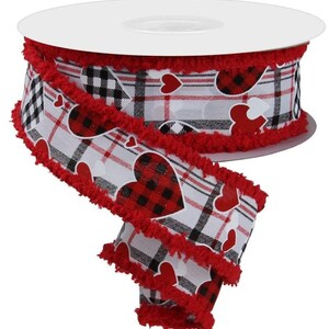 May include: A spool of decorative ribbon featuring a Valentine's Day theme. The ribbon has a white background with a plaid pattern and red hearts. The edges are trimmed with red, fuzzy material.