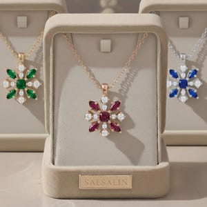 May include: Three snowflake pendant necklaces in display boxes. One has a gold chain and pendant with green and white stones. Another has a rose gold chain and pendant with red and white stones. The third has a silver chain and pendant with blue and white stones. The brand name "SALSALIN" is visible.