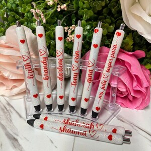 May include: Set of eight white glitter pens with red hearts and personalized names, including "Tony & Erin", "Gina", "Ms. Julie", "Super Para", "Darlene", "Brandy", "Lyzette", and "Shavonna".