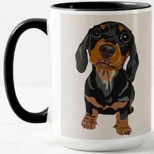 May include: White ceramic mug with a black handle and rim. The mug features a cartoon illustration of a black and brown dachshund dog. The dog has large eyes and is centered on the mug.