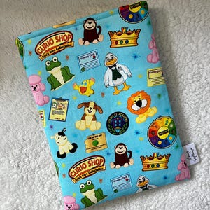 Puede incluir: Una bolsa de tela azul con un patrón repetido de animales de dibujos animados y el texto "CURIO SHOP Arte's Rare Collectables".