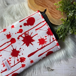 May include: A white fabric laptop sleeve with a red blood splatter pattern. The sleeve has a black zipper and the text "Always September" printed on the front.