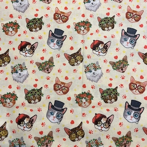 May include: A cream-colored fabric with a repeating pattern of cats wearing various accessories. The cats are wearing hats, glasses, flowers, and berets. The background is a light cream color with red hearts and paw prints.